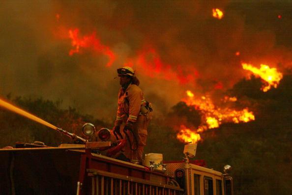 A firefighter battles a portion of the Cedar Fire using a water spout from atop a firetruck October 27, 2003 near Lakeside in San Diego, California.